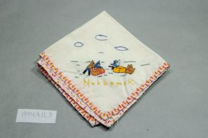 Image of Figures rolling barrel and sitting on box with the word "Nakkomek" below, one of a set of 3 embroidered napkins, each with different scene and title
